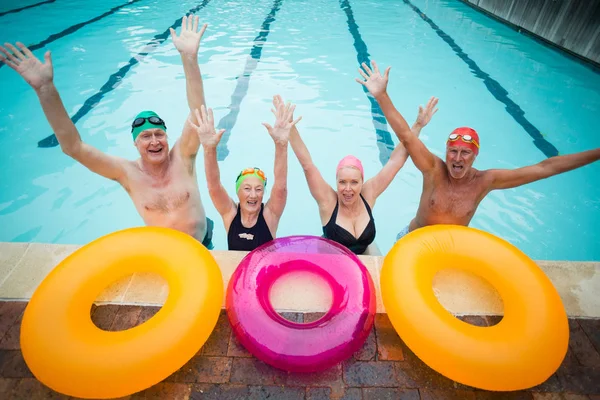 Cheerful senior swimmers with inflatable rings at poolside — Stock Photo, Image