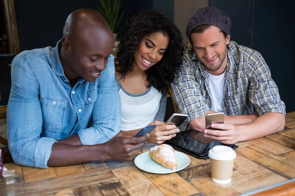 Amigos usando telefones inteligentes à mesa — Fotografia de Stock