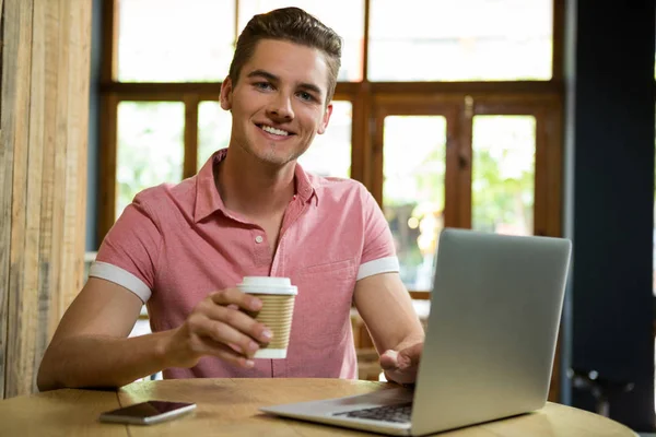 Hombre usando el ordenador portátil mientras toma café en la cafetería — Foto de Stock