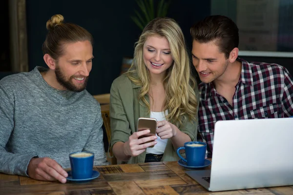 Amigos usando el teléfono inteligente en la mesa en la cafetería — Foto de Stock