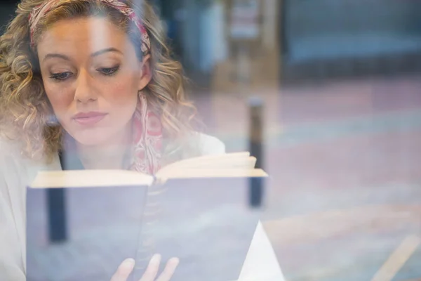 Kobieta czytająca książkę postrzegane przez okno kawiarni — Zdjęcie stockowe