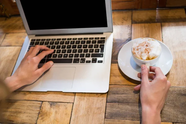 Frau hält Kaffeetasse während sie Laptop benutzt — Stockfoto