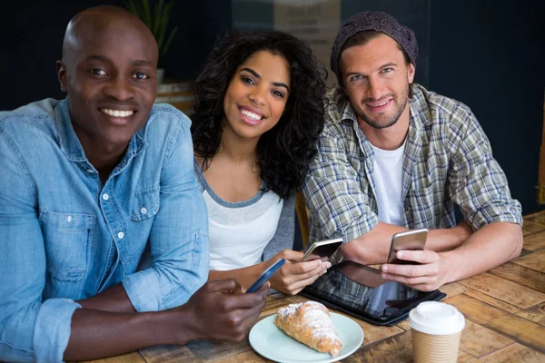 Amigos sorridentes segurando telefones inteligentes à mesa — Fotografia de Stock