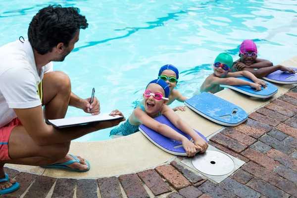 Instructor escribiendo en portapapeles con nadadores junto a la piscina —  Fotos de Stock