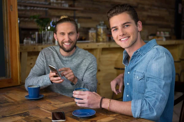 Улыбающиеся мужчины, сидящие за столом в кафе — стоковое фото