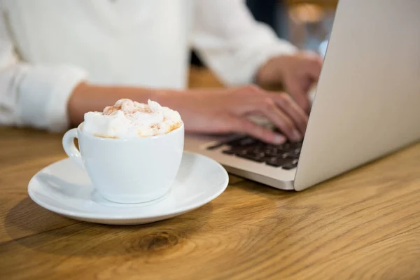 Frau benutzt Laptop bei Kaffee mit Schaum auf Tisch — Stockfoto