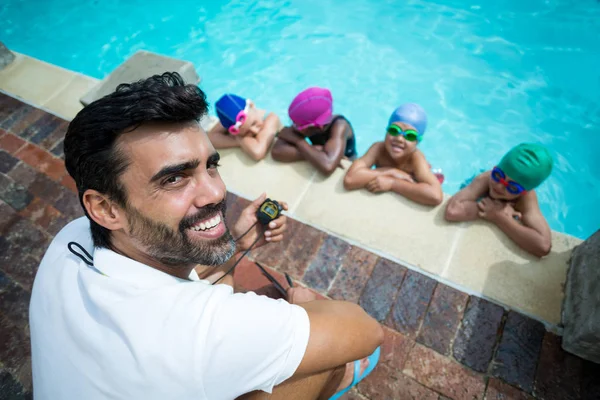 Instrutor que utiliza cronômetro com pequenos nadadores à beira da piscina — Fotografia de Stock