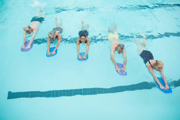 Senior swimmers and trainer swimming with kickboards — Stock Photo, Image