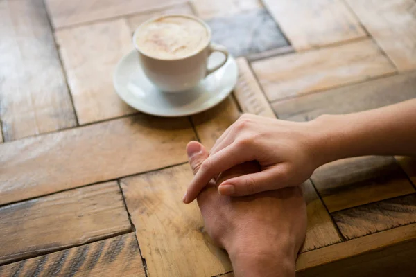 Ζευγάρι κρατώντας τα χέρια με φλιτζάνι καφέ στο τραπέζι — Φωτογραφία Αρχείου