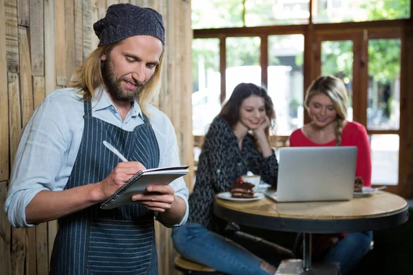 Αρσενικό barista γράφοντας παραγγελίες με στους θηλυκούς πελάτες — Φωτογραφία Αρχείου