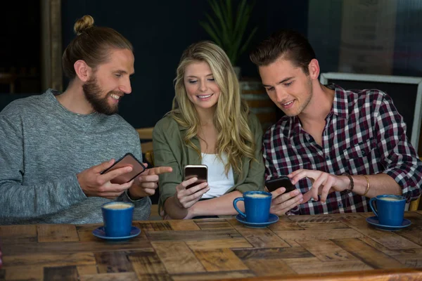 Друзья, использующие смартфоны за столом в кафе — стоковое фото