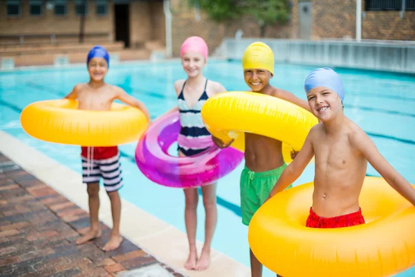 Amigos que carregam anéis infláveis na beira da piscina — Fotografia de Stock