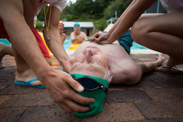Lifeguards pressing chest of unconscious man at poolside — Stock Photo, Image