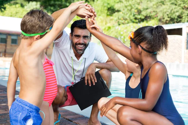 Niños apilando manos con entrenador en la piscina — Foto de Stock