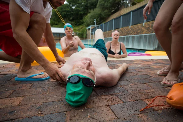 Lifeguards and friends looking at unconscious man at poolside — Stock Photo, Image