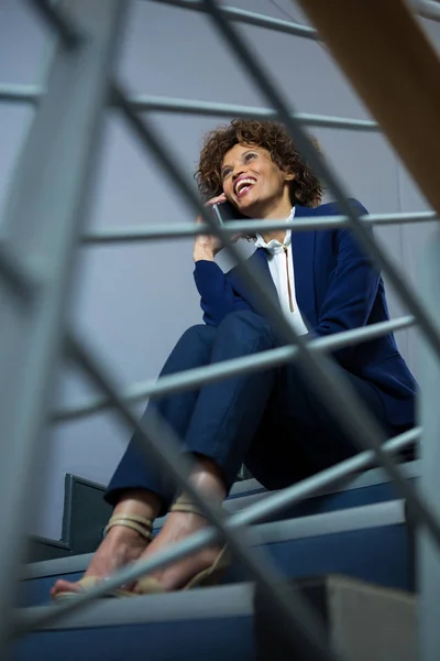 Businesswoman talking on mobile phone while sitting on steps — Stock Photo, Image
