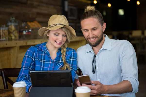 Pareja usando el teléfono móvil en la mesa en la cafetería —  Fotos de Stock