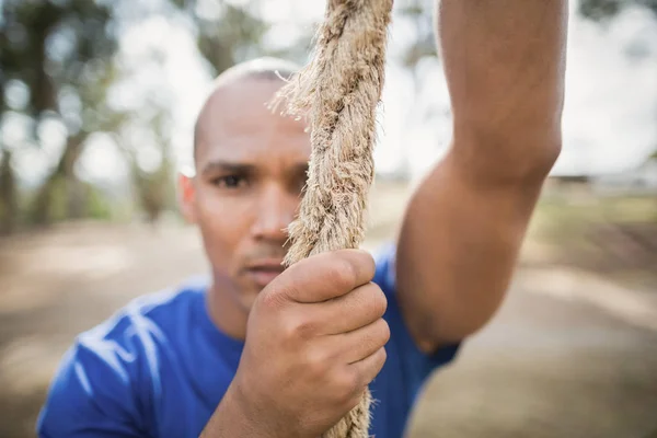 Fit man climbing rope during obstacle course — Stock Photo, Image