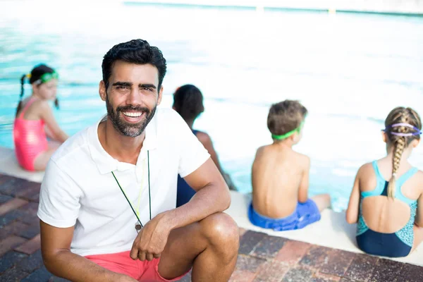 Istruttore maschio accovacciato dai bambini a bordo piscina — Foto Stock