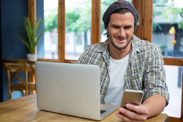 Sorrindo homem usando telefone celular e laptop no café — Fotografia de Stock