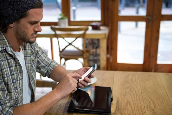 Młody człowiek za pomocą inteligentnego telefonu przy stoliku w kawiarni — Zdjęcie stockowe