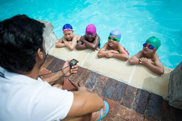 Instructeur utilisant un chronomètre pendant l'entraînement de petits nageurs au bord de la piscine — Photo