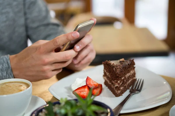 Чоловік використовує мобільний телефон з кавою і десертом — стокове фото