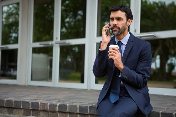 Affärsman holding disponibla kaffekopp talar på mobiltelefon — Stockfoto