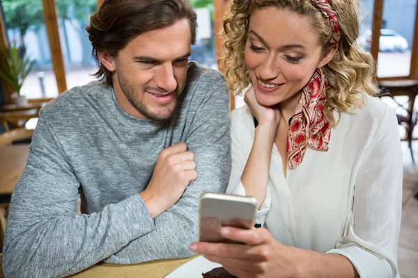 Par med hjälp av mobiltelefon vid bord i café — Stockfoto