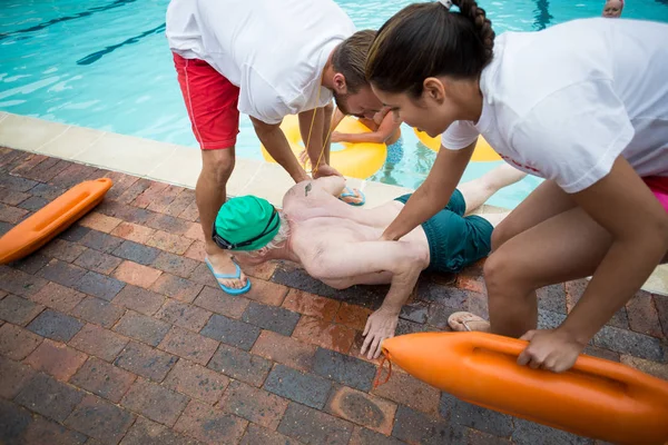 Ναυαγοσώστες βοηθώντας ασυνείδητο ανώτερος άνθρωπος δίπλα στην πισίνα — Φωτογραφία Αρχείου