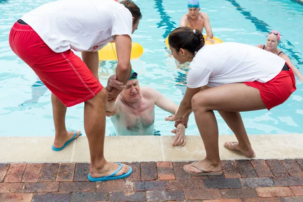 Bagnini aiutare inconscio anziano uomo in piscina — Foto Stock