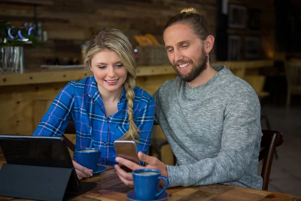 Pareja usando el teléfono celular en la mesa en la cafetería —  Fotos de Stock