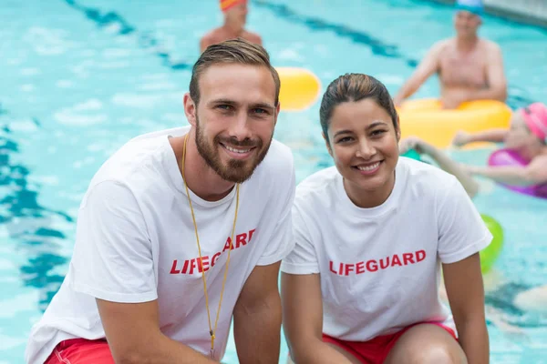 Male and female lifeguards crouching at poolside — Stock Photo, Image