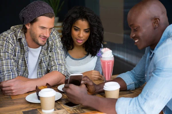 Man showing smart phone to friends at table — Stock Photo, Image