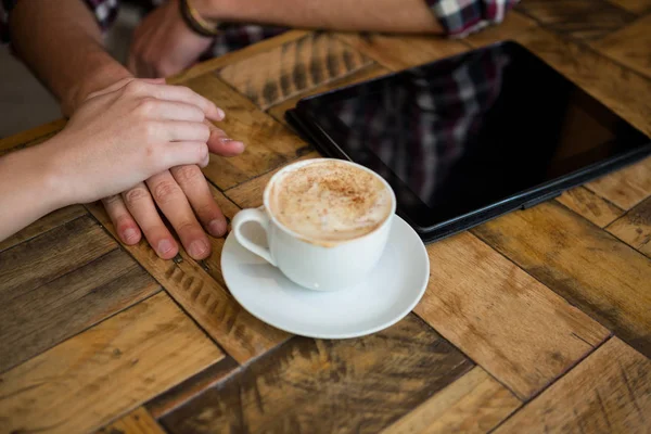 Pasangan berpegangan tangan dengan cangkir kopi dan tablet PC — Stok Foto