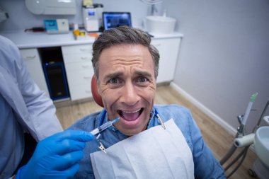 Dentist injecting anesthetics in scared patient mouth clipart