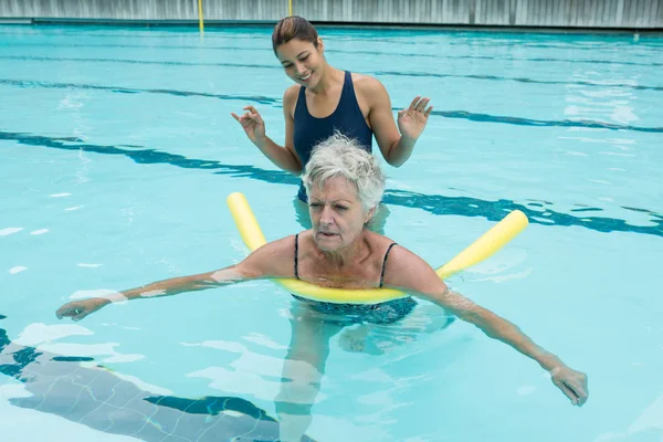 Тренер-женщина помогает пожилой женщине в бассейне — стоковое фото