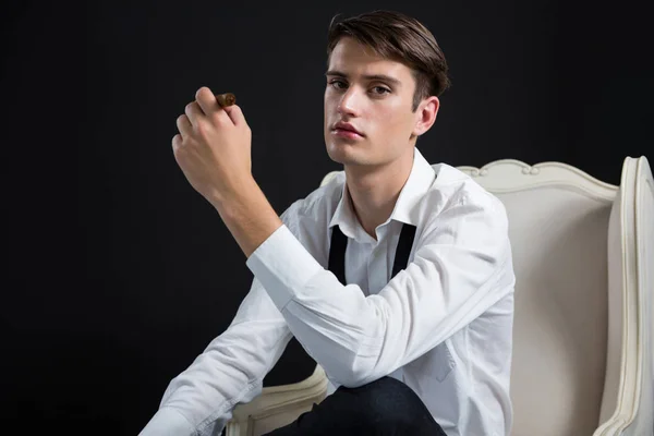 Androgynous man sitting on chair with cigar