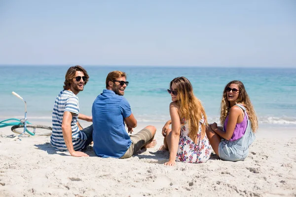 Веселые друзья сидят на берегу в солнечный день — стоковое фото