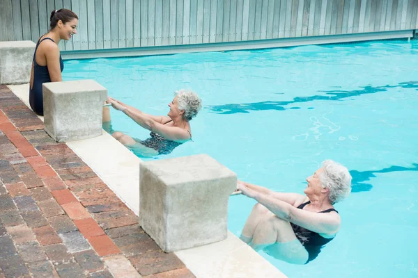 Treinador interagindo com mulheres idosas na piscina — Fotografia de Stock