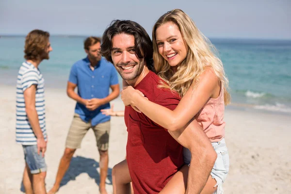 Novio piggybacking novia por amigos en la playa — Foto de Stock