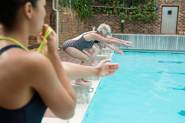 Trainer fluiten terwijl senior vrouwen duiken in zwembad — Stockfoto