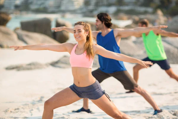 Friends practicing warrior 2 pose on shore — Stock Photo, Image