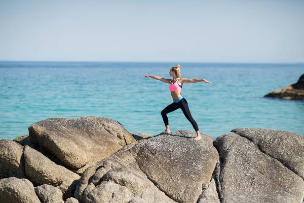 Mujer practicando la pose guerrera en la costa rocosa —  Fotos de Stock