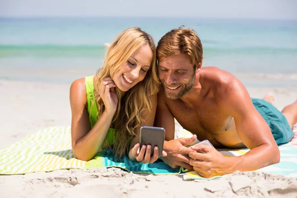 Couple looking in phone while lying at beach — Stock Photo, Image