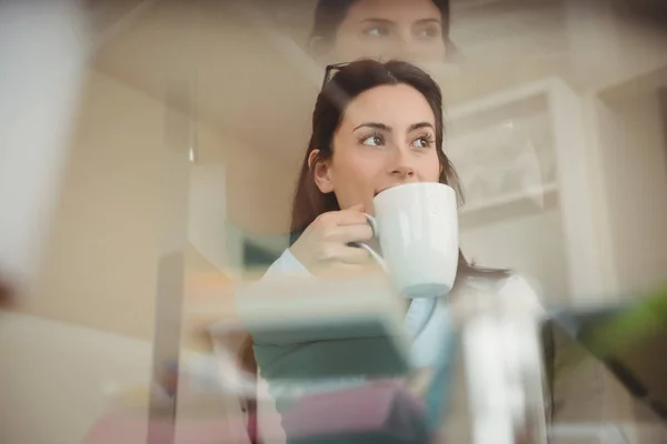 Жінка п'є каву, сидячи за скляним столом — стокове фото