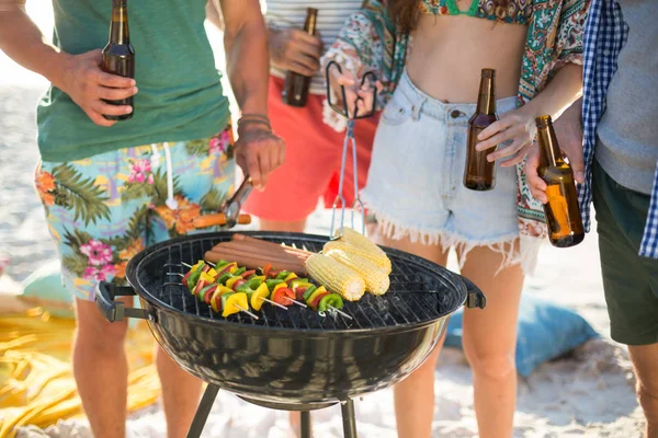 Friends having drinks by barbecue on shore — Stock Photo, Image