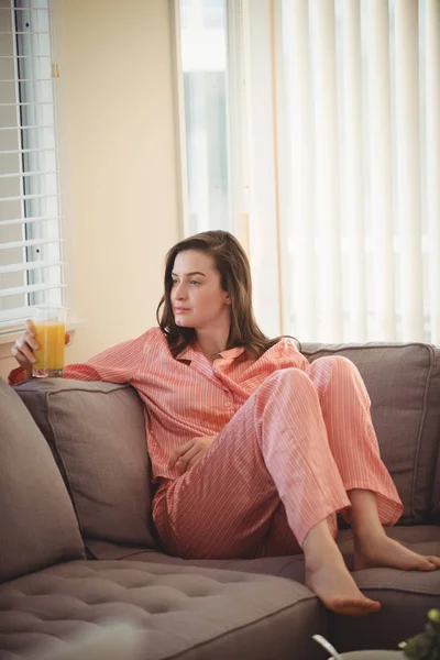 Woman holding juice while sitting on sofa — Stock Photo, Image