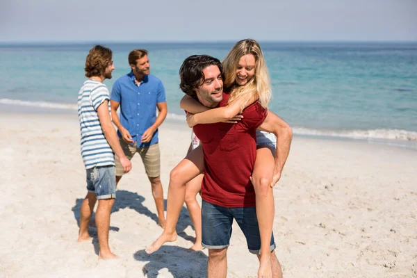 Człowiek, piggybacking dziewczyna przez przyjaciół z plaży — Zdjęcie stockowe