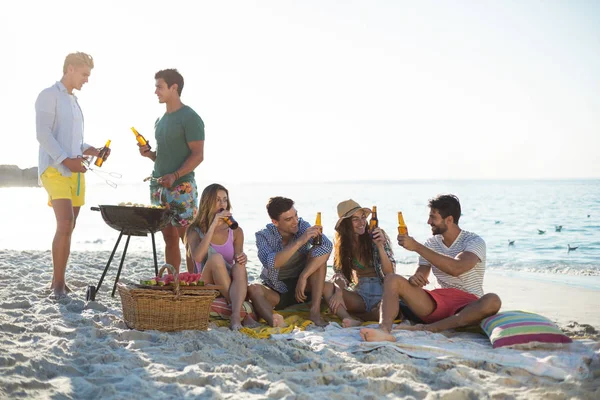 Friends having drinks by barbecue at beach — Stock Photo, Image